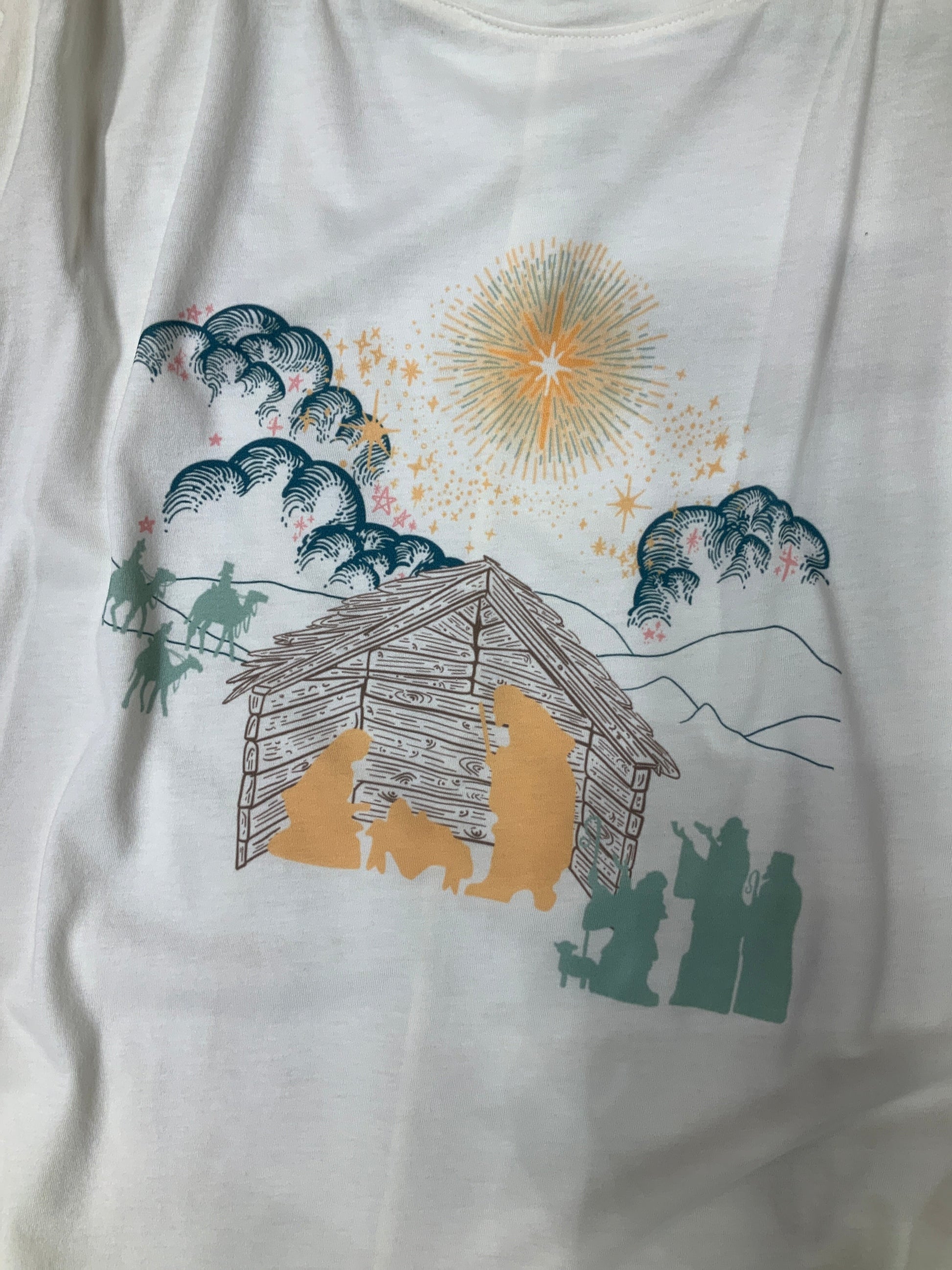 White T Shirt depicting a nativity scene. Green clouds Gold Stars. Yellow Mary Joseph and baby Jesus silhouette, all other silhouettes are light teal